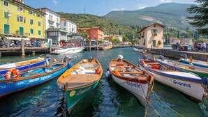 A marina with several boats docked, a small building with a sign, and a mountainous backdrop. - Il Giardino In Montagna Family Friendly (Tenno)