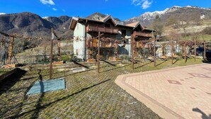 A chalet-style building with a wooden balcony, surrounded by mountains and a clear sky. - Il Giardino In Montagna Family Friendly (Tenno)