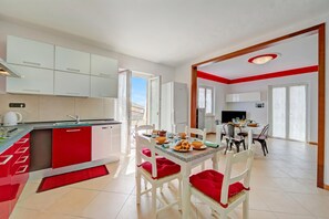 A modern kitchen with white cabinets, a dining area with white chairs and red cushions, and a view of the outdoors. - Il Giardino In Montagna Family Friendly (Tenno)