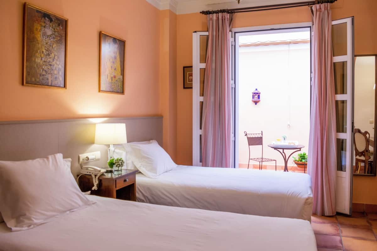 A hotel room with two beds, a nightstand with a lamp, a telephone, and a small table with a plant.