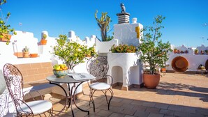 An outdoor patio with a table and chairs, surrounded by potted plants and a decorative bird statue. - Hotel Veracruz (Utrera)