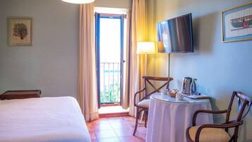 A hotel room with a bed, a table with chairs, a TV mounted on the wall, and a balcony with curtains.
