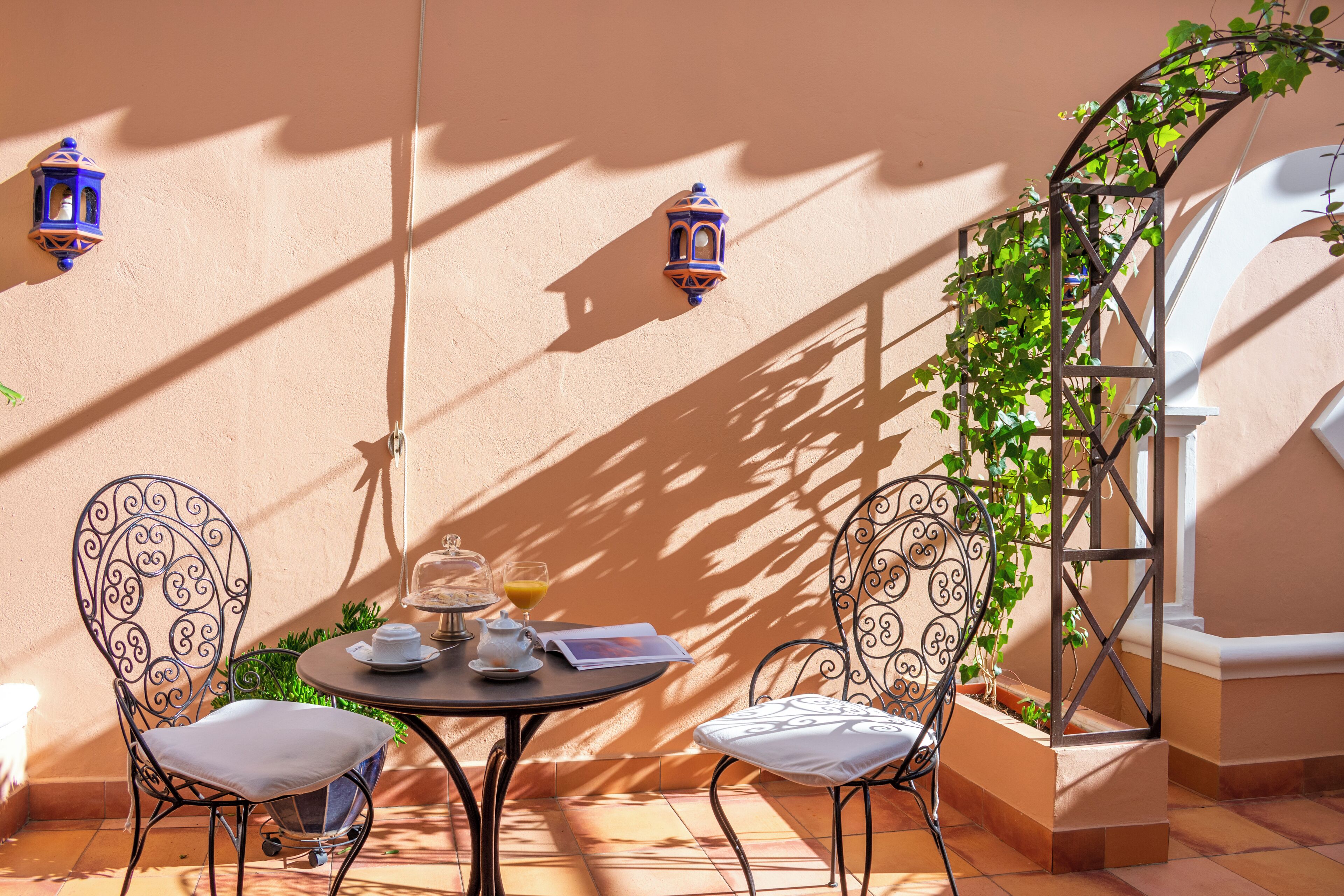 Een zonnig terras met een ronde tafel, twee sierlijke stoelen en een kleine plant.
