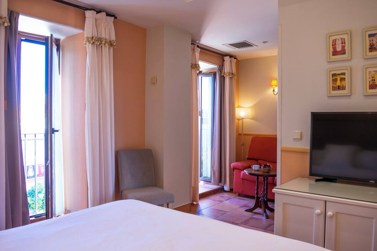 A hotel room with a bed, a TV, a desk, and a chair. There are curtains and a lamp.