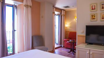 Habitación de hotel con cama, televisor, escritorio y una silla. Hay cortinas y una lámpara.