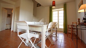 Ein Essbereich mit einem weißen Tisch und Stühlen, einer Treppe und einem Fenster mit grünen Vorhängen.