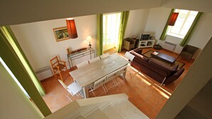 Ein Essbereich mit Tisch und Stühlen, einer Couch, einem Fernseher und einem Fenster mit Vorhängen.