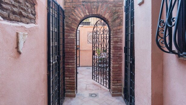 Um beco estreito com um arco de tijolos e portões de metal preto.