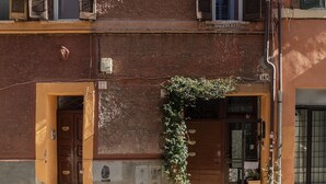 Um edifício com fachada de tijolos, porta de madeira e um pequeno jardim com plantas.