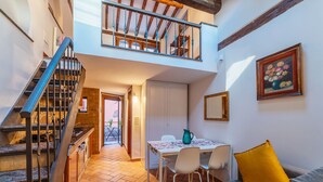 Um espaço de estar compacto com uma escada que dá para um andar superior, uma área de jantar com mesa e cadeiras, e um sofá com almofada.