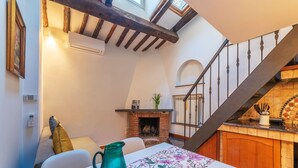 Um quarto acolhedor com lareira, uma mesa com toalha de mesa florida, um vaso verde e uma escada com corrimão de madeira.