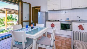 A compact kitchen with white cabinets, a refrigerator, and a microwave. There is a dining table with chairs and a small outdoor seating area with a table and chairs. - Lavender by Interhome (Pomaia)