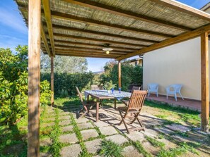 Un portico riparato con tavolo e sedie, immerso nel verde e con un vialetto in pietra.