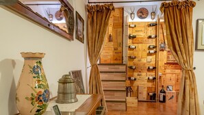 Una habitación con una escalera de madera, una pared llena de botellas de vino, un jarrón decorativo y un reloj digital.