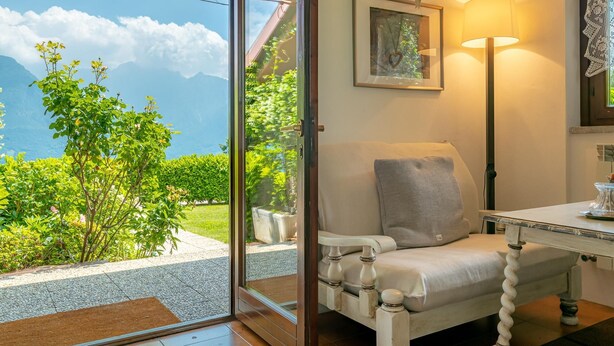 Una habitación con vistas a montañas y vegetación, un sillón blanco, una mesa y una lámpara.