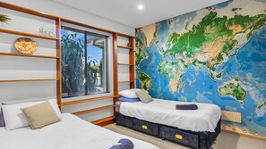 Une chambre à coucher avec un lit, une fenêtre avec des stores, une bibliothèque et une grande carte du monde accrochée au mur.
