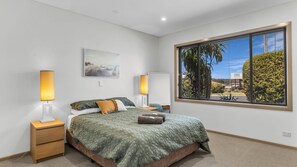 Una camera da letto moderna con una grande finestra, un letto con copripiumino verde, due abat-jour, un comodino e un quadro appeso al muro.