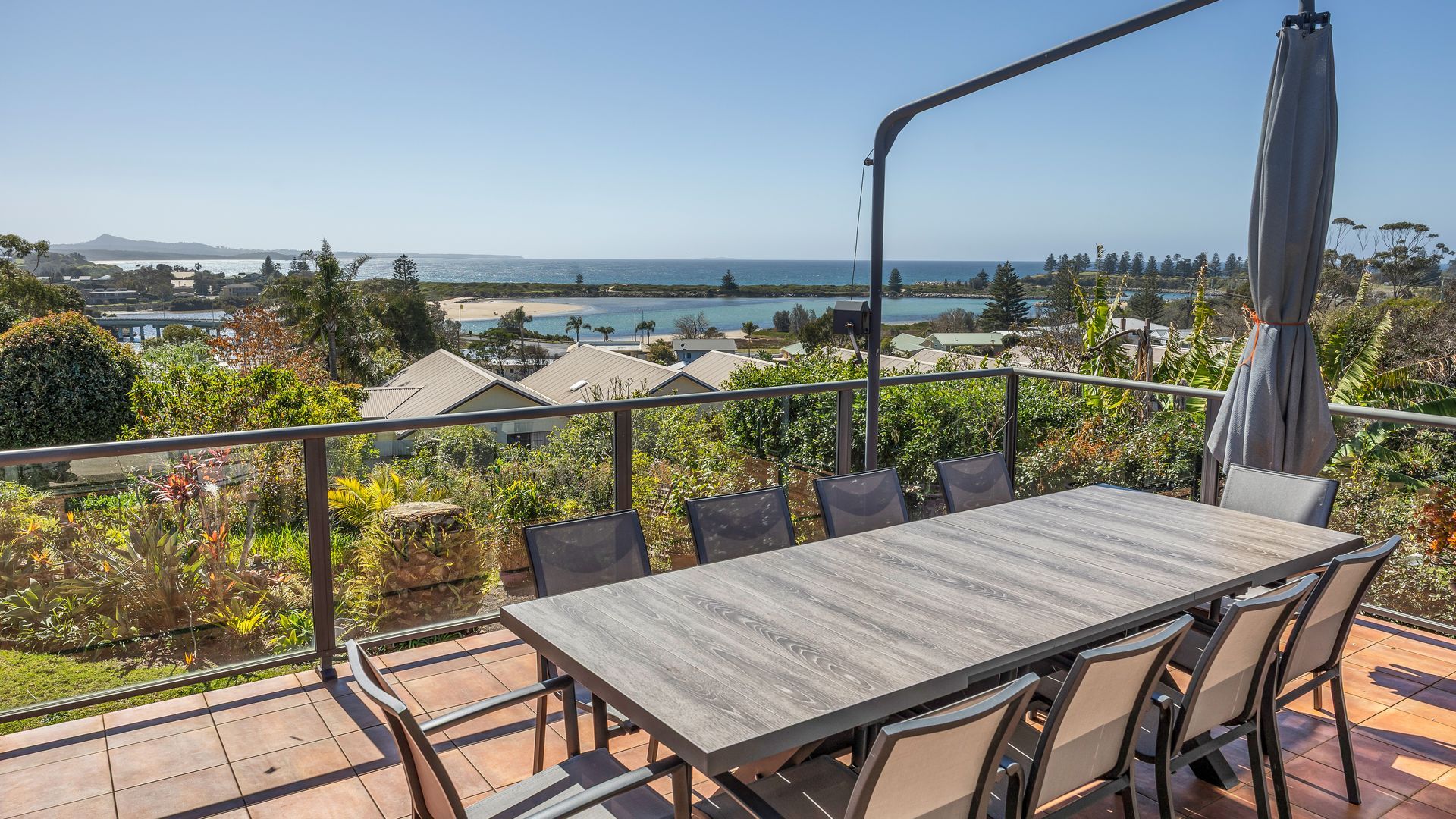 A terrace with a table and chairs, overlooking a coastal landscape with houses and a beach.