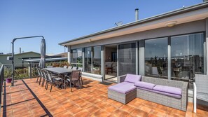 Un patio extérieur moderne comprenant une table et des chaises, un canapé en osier et un espace de vie fermé par des parois de verre.