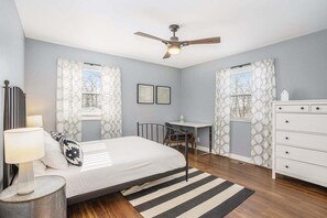 Un dormitorio con cama, escritorio, cómoda y ventilador de techo.