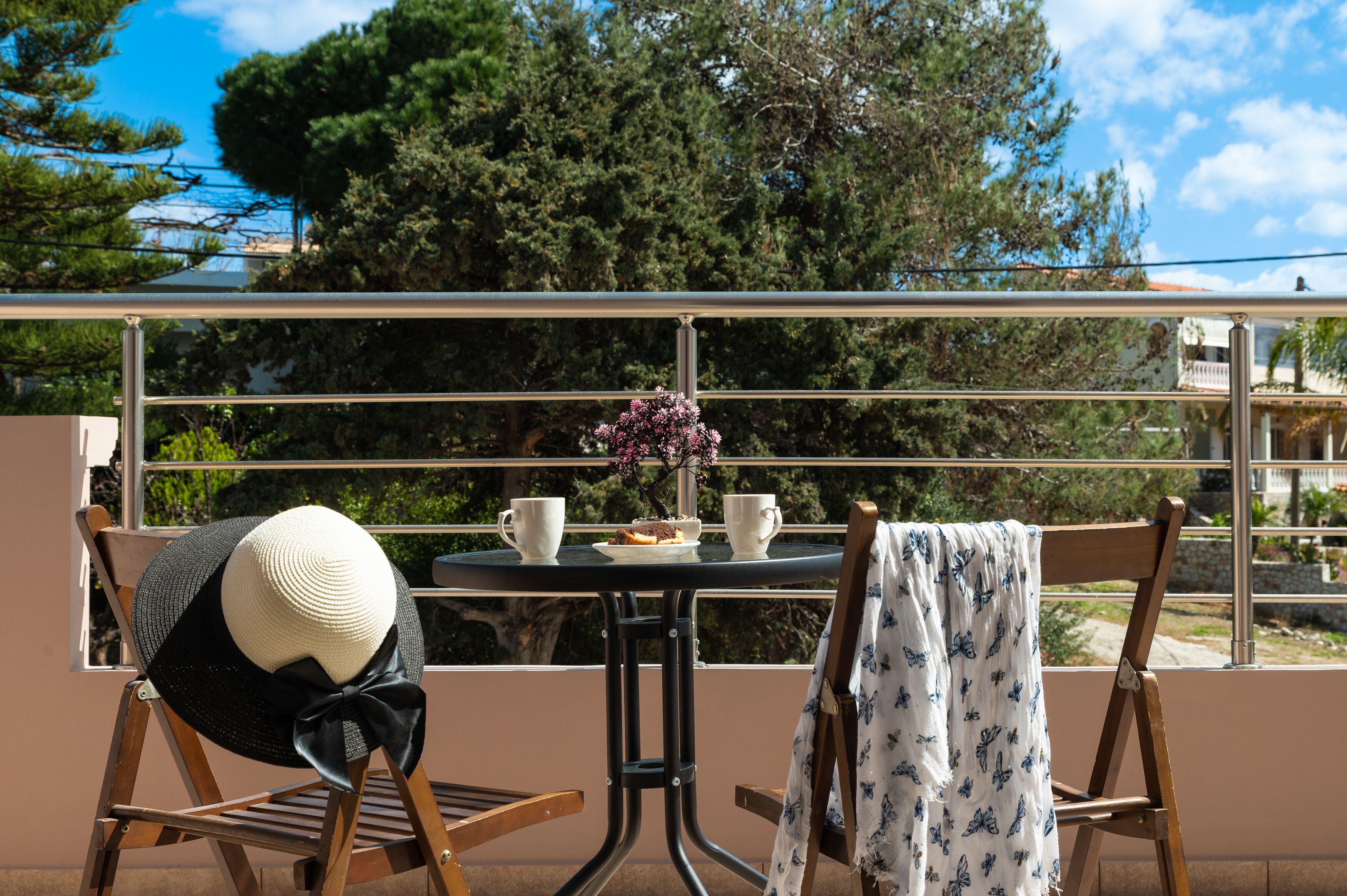 Uma varanda com mesa, cadeiras, um chapéu e um vaso com flores.