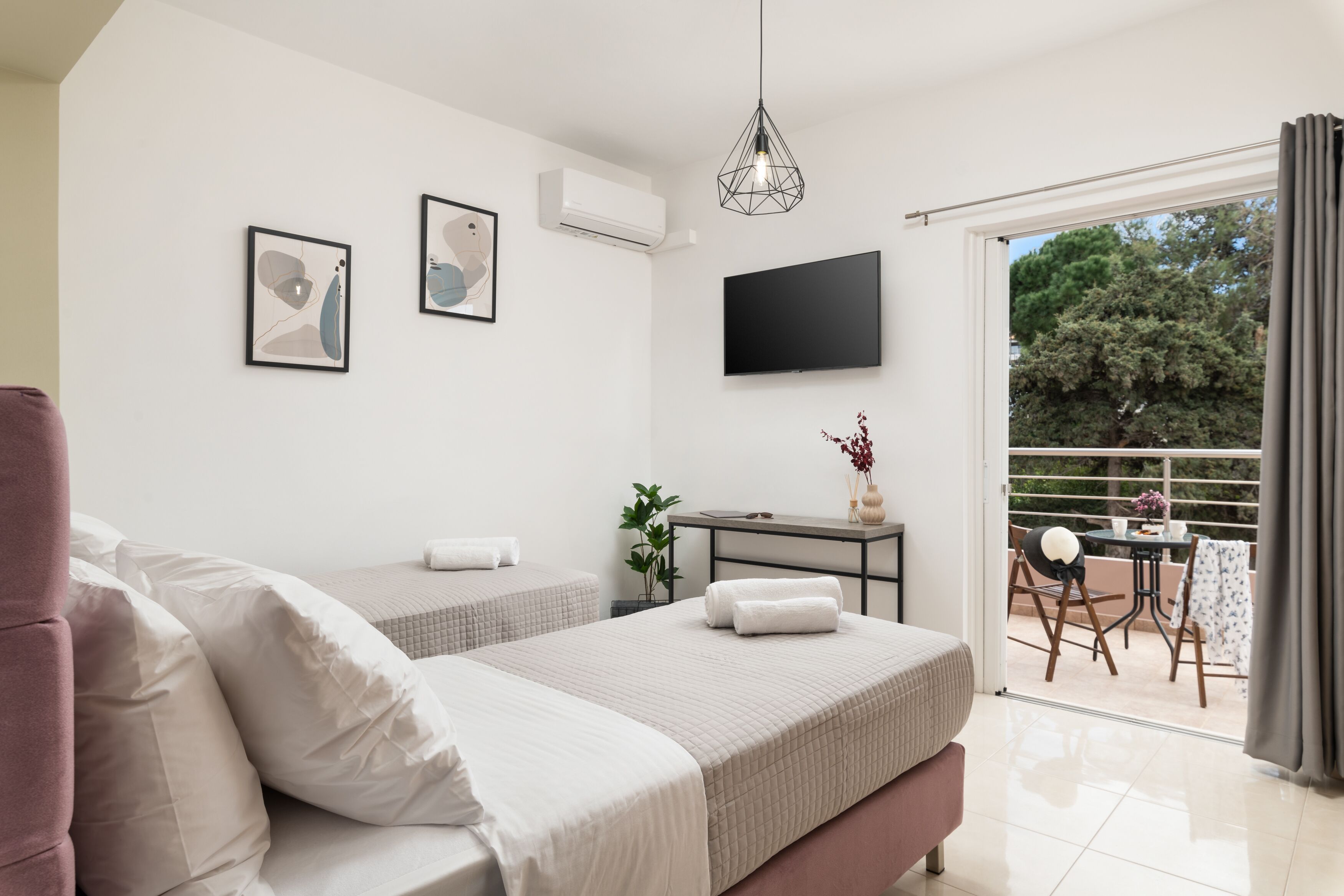 A modern bedroom with two beds, a flat-screen TV, and a balcony with a table and chairs.
