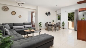A modern living room with a sectional sofa, a dining area with a table and chairs, and a kitchen with a refrigerator and cabinets. - The cozy nook (Chorafakia)