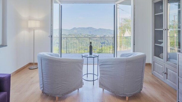 Een moderne kamer met balkon, twee grijze fauteuils, een klein rond tafeltje en een vloerlamp.