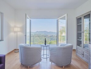 Een moderne kamer met balkon, twee grijze fauteuils, een klein rond tafeltje en een vloerlamp.