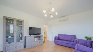 Een woonkamer met een televisie, een paarse bank en een kast met glazen deuren.