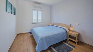 Een slaapkamer met een bed, nachtkastje met lamp, raam en een plafondlamp.