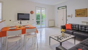 Een moderne woonkamer met een eethoek, een bank, een televisie en uitzicht op de omgeving.