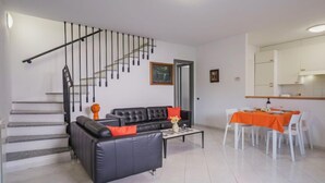 Een moderne woonkamer met een zwarte leren bank, een salontafel en een eethoek met een tafel en stoelen.