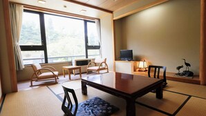 A traditional Japanese room with tatami flooring, a low table, two cushioned chairs, a television, and a decorative bird statue. - Hijiori Onsen Kangetsu (Okura)