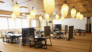 A spacious dining area with multiple tables and chairs, traditional paper lanterns hanging from the ceiling, and a large screen on the wall. - Hijiori Onsen Kangetsu (Okura)