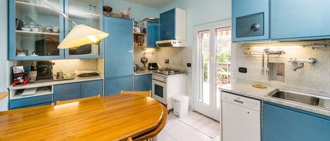 A kitchen with blue cabinets, a wooden dining table, and a dishwasher.