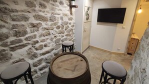 Ein rustikaler Raum mit Stehwänden, einem Holzfass, zwei Hockern, einem Wand-Fernseher und einer kleinen Pflanze an der Wand.