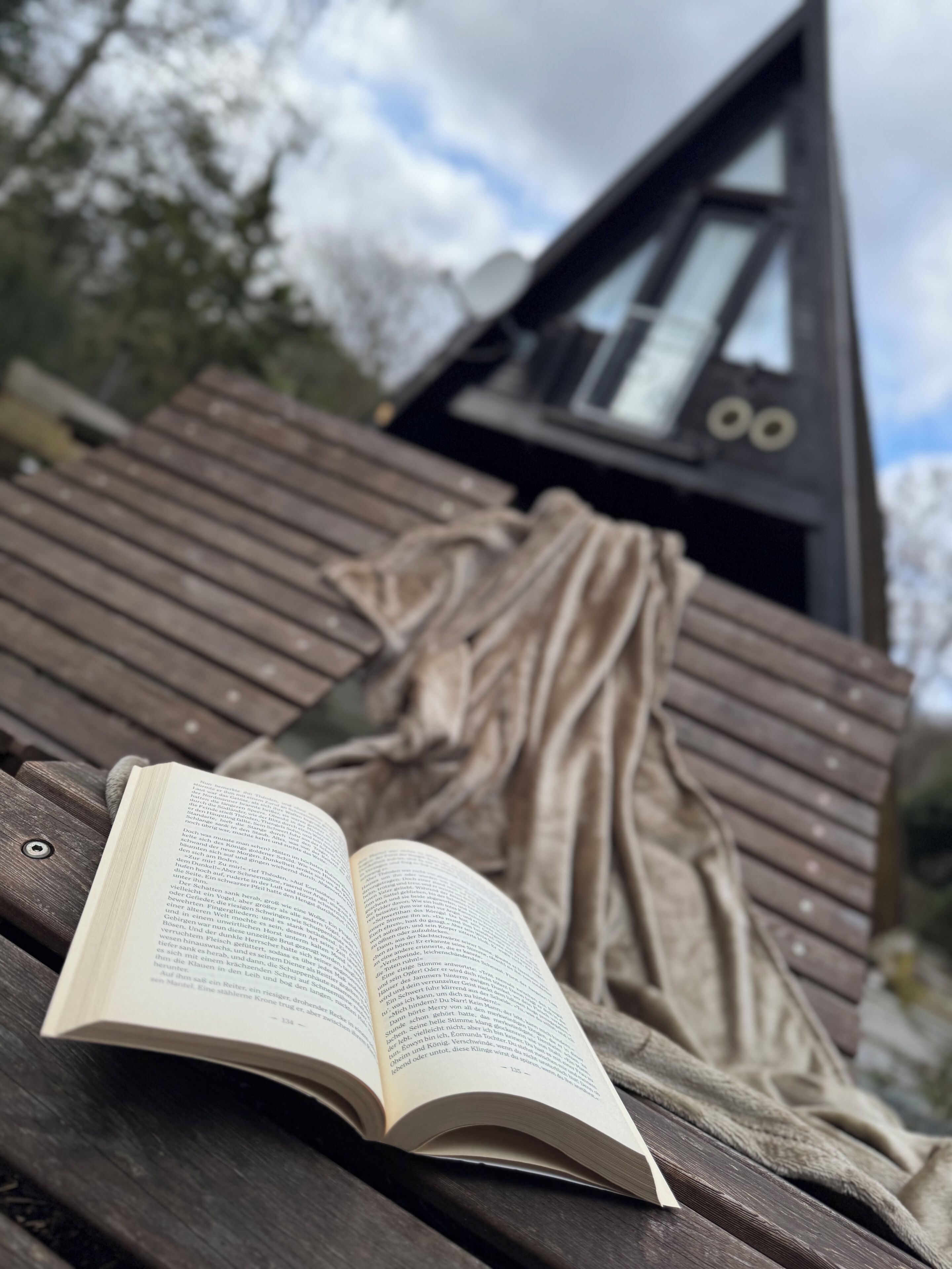 Un libro abierto sobre una superficie de madera, un banco de madera y un edificio triangular con una ventana.