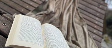 Un libro abierto sobre una superficie de madera, un banco de madera y un edificio triangular con una ventana.