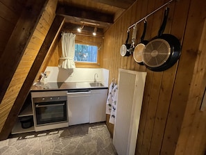 Pieni, käytännöllinen keittiö, jossa on liesi, pesuallas ja ikkuna, jossa on verhot.