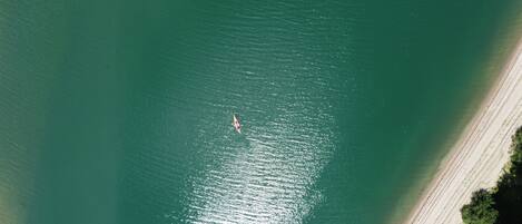 Vue aérienne d’une plage avec un seul kayak sur l’eau et une rive sablonneuse.