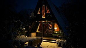 Une petite cabane triangulaire et accueillante, avec une façade en bois, une véranda et un banc.
