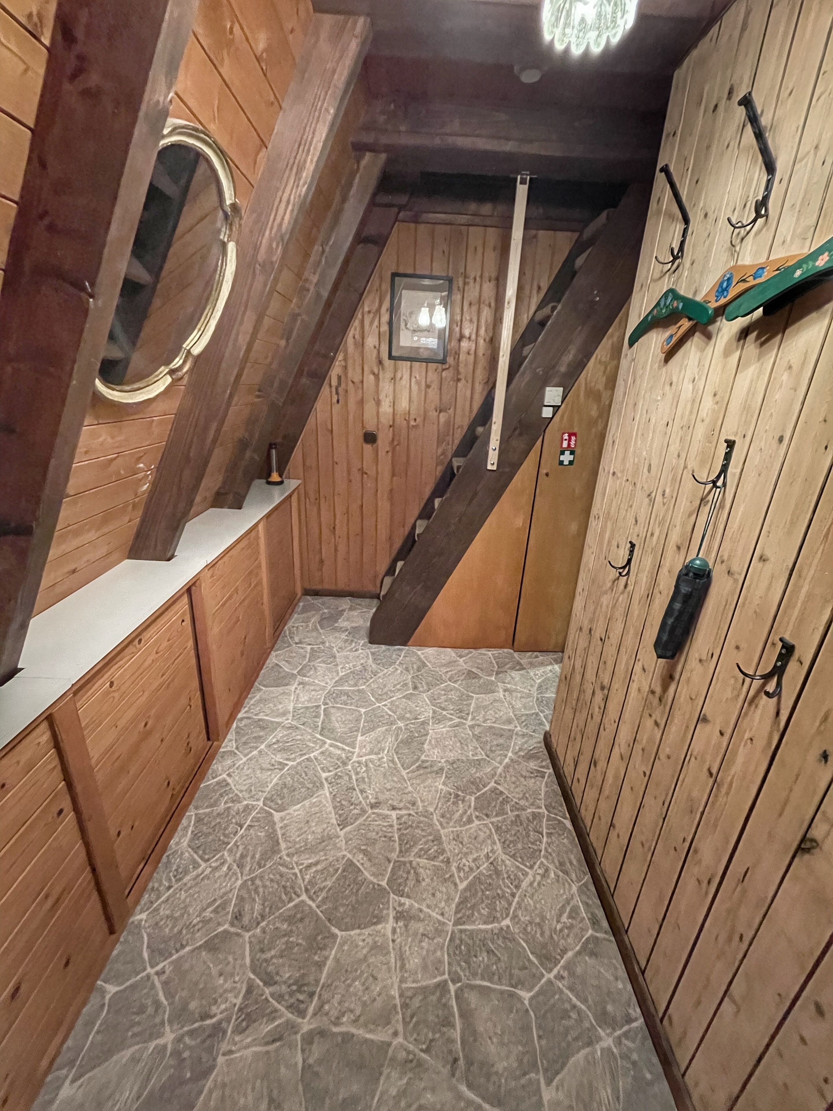 A wooden interior with a stone floor, a staircase, and a mirror on the left.