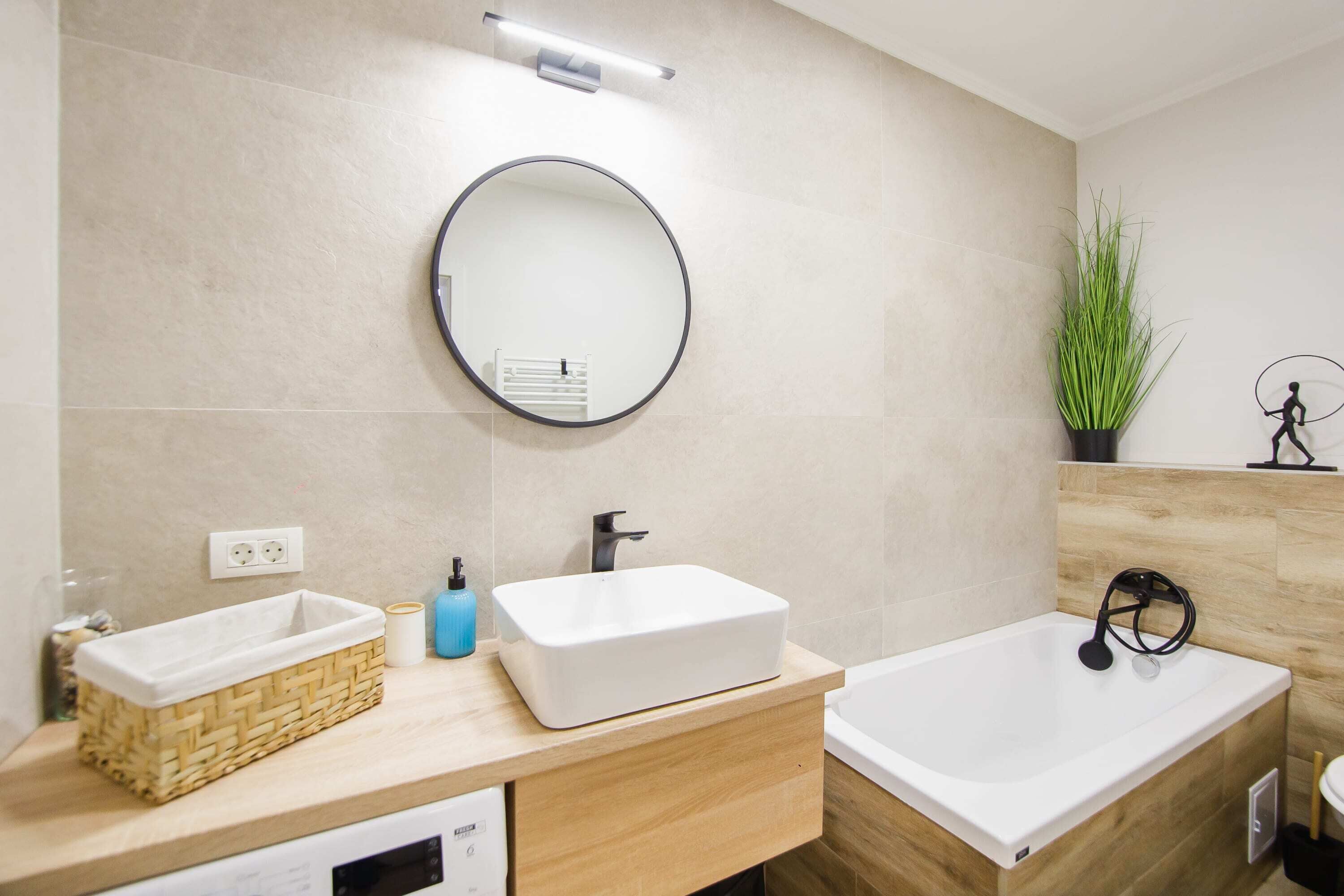 A modern bathroom with a rectangular sink, a round mirror, a bathtub, and a small potted plant.