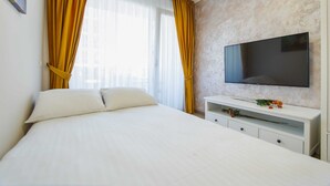 A hotel room with a bed, a TV on a white console, and a window with yellow curtains. - Cappuccino Colors at West Residence (Oradea)