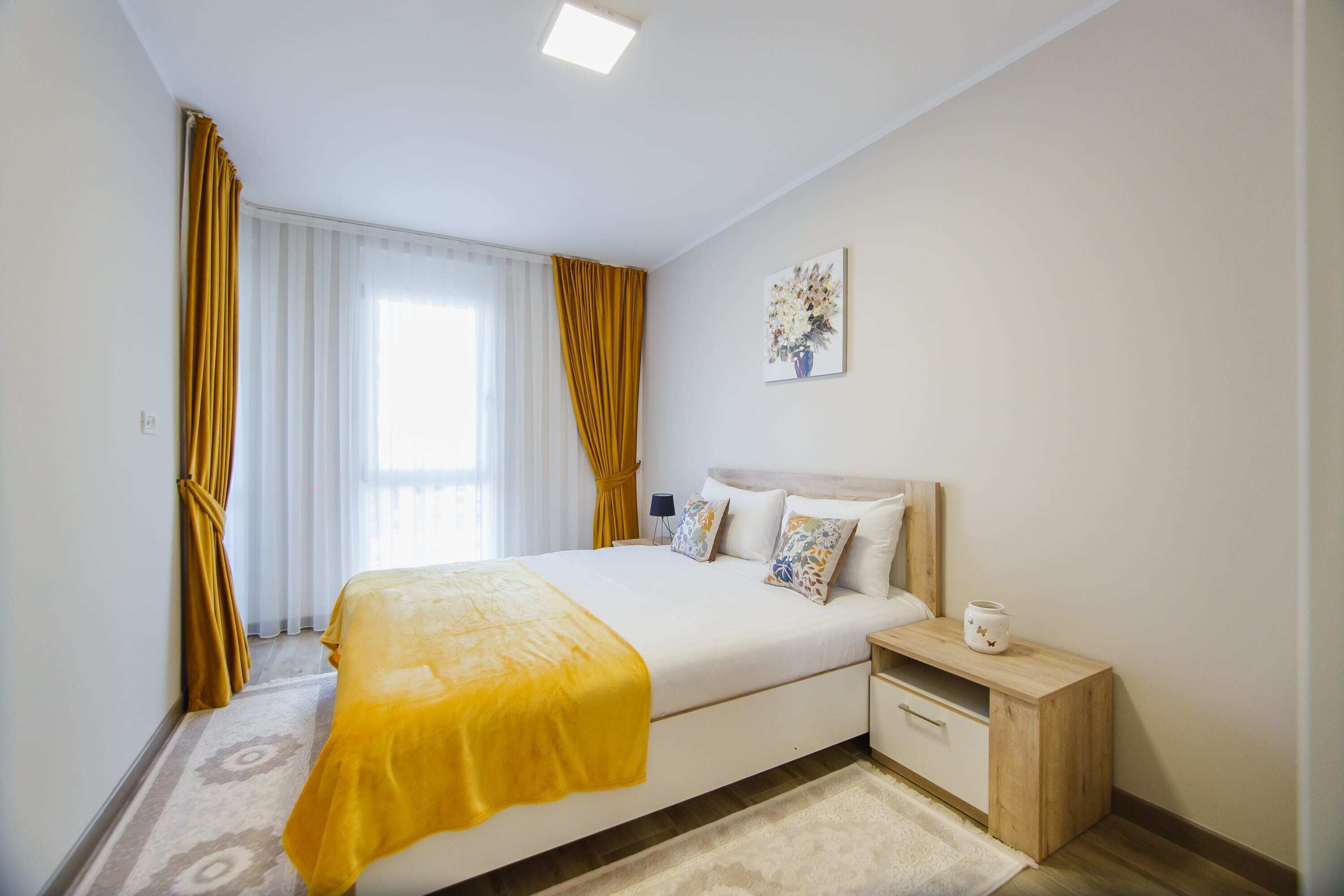 Una habitación de hotel con una cama grande, una mesita de noche con lámpara, un pequeño atril y una ventana con cortinas.