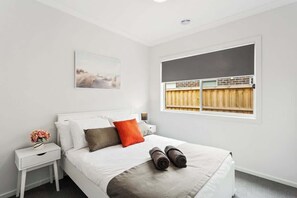 Habitación de hotel con cama, mesita de noche, ventana con persianas y una obra de arte colgada en la pared.
