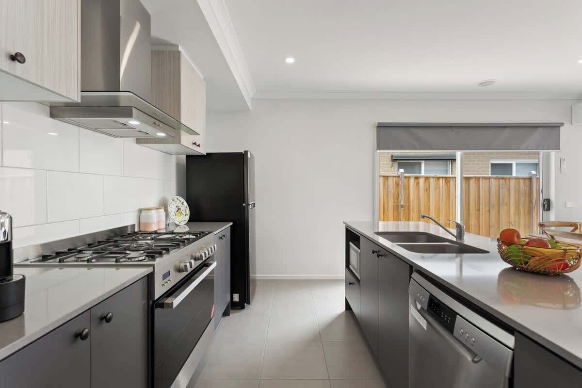 A modern kitchen with stainless steel appliances, a dishwasher, and a wooden fence visible through the window.