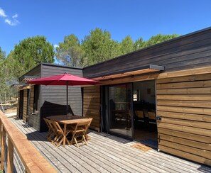 A wooden deck with a table and chairs, a red umbrella, and a sliding glass door leading to an interior space.