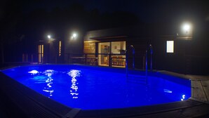 A swimming pool with a wooden deck, a covered seating area, and a building with large windows. - New Ecogîte in the countryside, three minutes from all amenities. (Limoux)